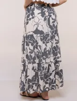 Falda maxi color crudo con estampado floral en tonos oscuros, tiro alto con cintura elástica fruncida, cordón de ajuste frontal y diseño escalonado de tres paneles con vuelo.