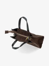 Cartera estructurada de formato cuadrado, confeccionada en gamuza color marrón tostado. Presenta doble asa de mano en cuero negro y correa larga regulable y desmontable en el mismo material. Incluye herrajes metálicos en tono bronce.