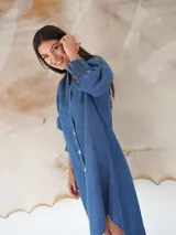 Vestido camisero de denim suave con cuello mao, cierre frontal con botones de nácar y mangas tres cuartos con puños elásticos fruncidos.
