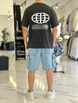 Remera negra con efecto gastado (acid wash), de corte oversize, con estampa frontal en blanco y celeste con la leyenda 'Stay Positive' y diseño gráfico de un globo terráqueo.