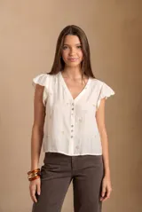 Blusa blanca sin mangas con escote en V, cierre frontal con botones y mangas con volados. Presenta pequeños bordados sutiles distribuidos por toda la prenda.