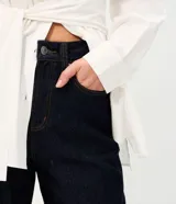 Pantalón de jean con corte new carrot, de cintura alta y estructura firme. Presenta un diseño holgado en la cadera que se estrecha hacia el bajo, con bolsillos funcionales y cierre frontal con botón y cremallera.