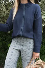 Campera tejida de punto con textura de rayas verticales, cierre frontal completo y cuello alto. Diseño de manga larga con hombros caídos.