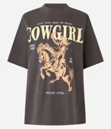 Remera de algodón con efecto lavado vintage, cuello redondo y mangas cortas. Presenta una estampa frontal contrastante con diseño de una mujer montando a caballo y lettering con la palabra Cowgirl.