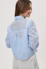 Camisa de manga larga con diseño de rayas verticales en tonos celestes, blancos y marrones, confeccionada en tejido semitransparente con cuello camisero y cierre frontal de botones.