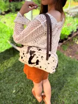 Cartera baguette de cuero color crudo con manchas negras, forro interno de tela y correa de cuero marrón.