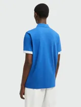 Polo de manga corta color azul, confeccionado en algodón. Presenta cuello clásico, cierre frontal con botones y detalles de franjas blancas en los bordes de las mangas. Incluye el parche con el logotipo de la marca en el pecho.