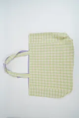 Bolso tipo tote de tela con estampado de cuadros vichy en tonos verde claro y blanco. Cuenta con dos asas de hombro reforzadas con forro interior en color lila.