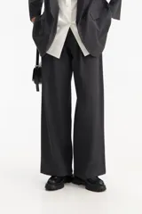 Pantalón de vestir gris oscuro, tiro bajo, con corte ancho y recto, pinzas delanteras y largo hasta el tobillo.