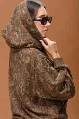 Buzo con capucha de calce relajado, con estampado animal print tipo piel de serpiente en tonos marrones. Presenta bolsillo frontal tipo canguro y cordones ajustables en contraste.