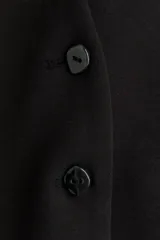 Blazer negro de punto grueso, corte entallado con hombros caídos, escote en V, cierre frontal de botones y bolsillos insertados decorativos.