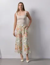 Pantalón capri de lino color crudo con estampado de hojas en tonos verdes, amarillos y naranjas. Presenta bolsillos laterales y detalle de puntilla en el ruedo.