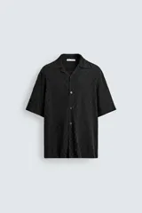 Camisa de corte relajado con cuello bowling y manga corta. Confeccionada en tejido fluido con textura jacquard de patrón geométrico y cierre frontal de botones.