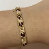 Pulsera artesanal confeccionada con cuentas Miyuki en tonos beige, dorado y detalles en rojo, con diseño ajustable.