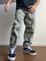 Pantalón de corte baggy con estampado de camuflaje digital en tonos grises y verdes. Presenta un diseño holgado y recto, ideal para un estilo urbano.