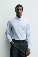 Camisa de corte slim fit confeccionada en tejido de algodón, color celeste. Cuenta con cuello abotonado, manga larga con puños ajustables mediante botón y cierre frontal con botonadura.