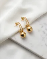 Caravanas colgantes de acero con baño de oro, compuestas por un gancho alargado y una esfera metálica lisa en el extremo inferior.