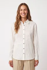 Camisa blanca de manga larga con bordados geométricos tono sobre tono, cuello camisero y cierre frontal de botones.