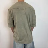 Remera de corte oversize en color verde oliva con efecto de lavado gastado. Presenta cuello redondo, mangas cortas con dobladillo ancho y costuras visibles.