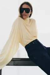 Jeans de tiro alto con corte flare y ajuste slim. Presenta trabillas en la cintura, bolsillos delanteros con detalle de botones metálicos y raya planchada a lo largo de las piernas. Cierre frontal con cremallera y botón.