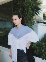 Blusa con cuello mao y mangas globo, confeccionada en algodón. La parte superior es de rayas azules y blancas, y la parte inferior es blanca con detalles de encaje.