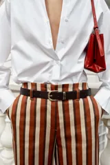 Pantalón de tiro alto y pernera recta con estampado de rayas verticales en tonos azul, marrón y beige. Incluye un cinturón delgado de color marrón oscuro con hebilla metálica dorada.