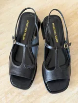 Sandalia de gamuza color marrón, con diseño tipo T-strap, taco cuadrado bajo y tira ajustable al talón con hebilla metálica dorada.