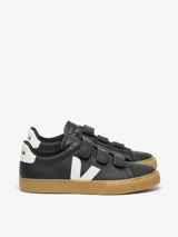 Zapatillas Veja modelo Recife, de cuero negro con cierre de tres tiras de velcro. Presenta el logo de la marca en blanco en el lateral, detalle blanco en el talón y suela de goma color caramelo.