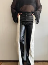 Pantalón largo de cuero sintético, corte recto, con diseño color block en blanco y negro.