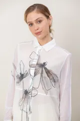 Camisa de microtúl translúcido color blanco marfil con estampado floral de estilo artístico abstracto en tonos oscuros, cuello camisero, manga larga con puños y cierre frontal abotonado.