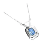Collar de cadena fina con dije rectangular de metal plateado y cristal facetado en color azul en el centro.
