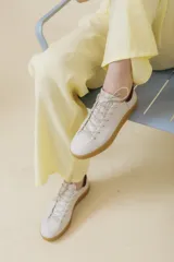 Zapatillas blancas de cuero vacuno con suela de caucho color caramelo y detalle en el talón color bordó. Cierre con cordones.