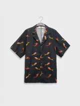 Camisa de manga corta con cuello estilo camper y estampado de sirenas en tonos naranja y amarillo. Tiene botones de madera y parche con logo. Corte boxy.