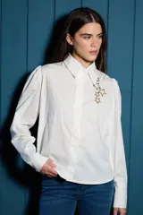 Camisa de corte clásico color blanco, con mangas largas abullonadas en los hombros y puños abotonados. Presenta un detalle de estrellas bordadas en color dorado sobre el lado izquierdo del pecho.