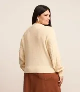 Suéter de punto pesado color crema, con cuello redondo y mangas largas. Presenta textura trenzada.