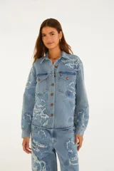 Sobrecamisa de denim azul con intrincados bordados florales en relieve, cierre frontal con botones metálicos y bolsillos delanteros con solapa.
