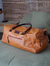 Bolso tipo weekender de cuero marrón, con asas de mano y bolsillo frontal con cierre metálico.