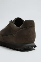 Zapatilla deportiva de hombre confeccionada en piel con acabado de serraje. Presenta un diseño de paneles combinados, cierre con cordones y suela dentada de goma.