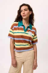 Remera tejida de algodón con diseño a rayas horizontales en tonos marrón, amarillo, verde y celeste. Presenta un corte boxy, cuello polo con escote en V y mangas cortas. Incluye una etiqueta decorativa en el pecho.
