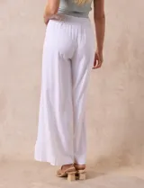 Pantalón blanco de lino con pretina ancha elastizada en punto smock, pierna ancha y ruedo con tajo.