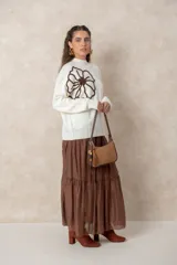 Cartera tipo baguette de diseño minimalista, confeccionada en una combinación de gamuza color beige en el panel frontal y cuero color chocolate en los bordes y la correa. Incluye un detalle colgante de cuentas de madera y cierre superior.