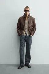 Sobrecamisa de corte relajado confeccionada en tejido efecto piel color marrón. Presenta cuello solapa, cierre frontal con cremallera, mangas largas con puños abotonados y dos bolsillos de plastrón con solapa en la parte frontal.