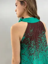 Blusa de satén con escote halter y cuello elevado anudado lateralmente. Presenta un diseño estampado degradado en tonos verde esmeralda y azul, con corte holgado y caída fluida.
