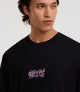 Remera negra de corte relajado, confeccionada en algodón, con cuello redondo y manga corta. Presenta un estampado gráfico en la espalda en color rosa que ilustra diversos tipos de hongos junto con la frase 'Microworld full of life'.