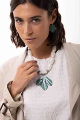 Collar corto con cuentas de acrílico en tono blanco nacarado y piedras naturales, con un medallón central en forma de hoja pintado a mano en color verde. Incluye cadena de acero quirúrgico para ajuste de largo.
