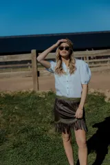 Minifalda color crema de cuero ovino con flecos y detalles en cuero marrón. Cierre frontal con cremallera. Estilo country.