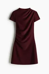 Vestido corto entallado de color bordó, con escote redondo y mangas cortas. Presenta un diseño con pliegues laterales en el hombro y la cintura que crean un efecto drapeado en el frente.