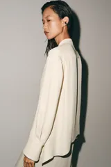 Blusa de viscosa color marfil, con cuello mao, manga larga con puños anchos, cierre frontal con botones y detalle de lazada colgante en el frente.