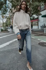 Chaqueta de textura bouclé en color crudo, con cuello subido, cierre frontal con cremallera, manga larga y puños elásticos.