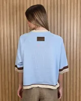 Buzo de punto color tostado, con mangas cortas holgadas y detalles de franjas en negro, blanco y beige en el cuello, los puños y el ruedo.